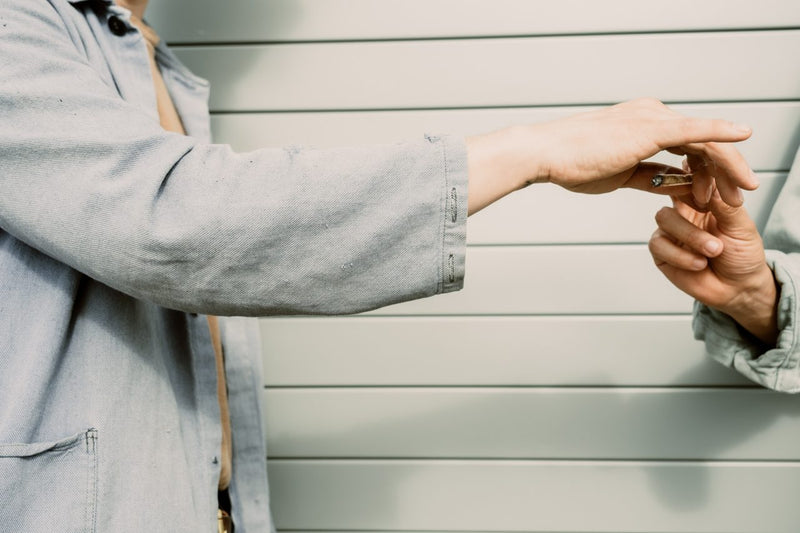 Two forearms in work jackets, one hand passing to the other against grey siding